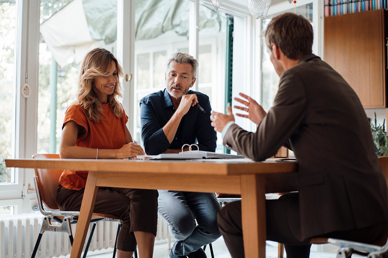 Smiling mature couple discussing over documents with real estate agent at table